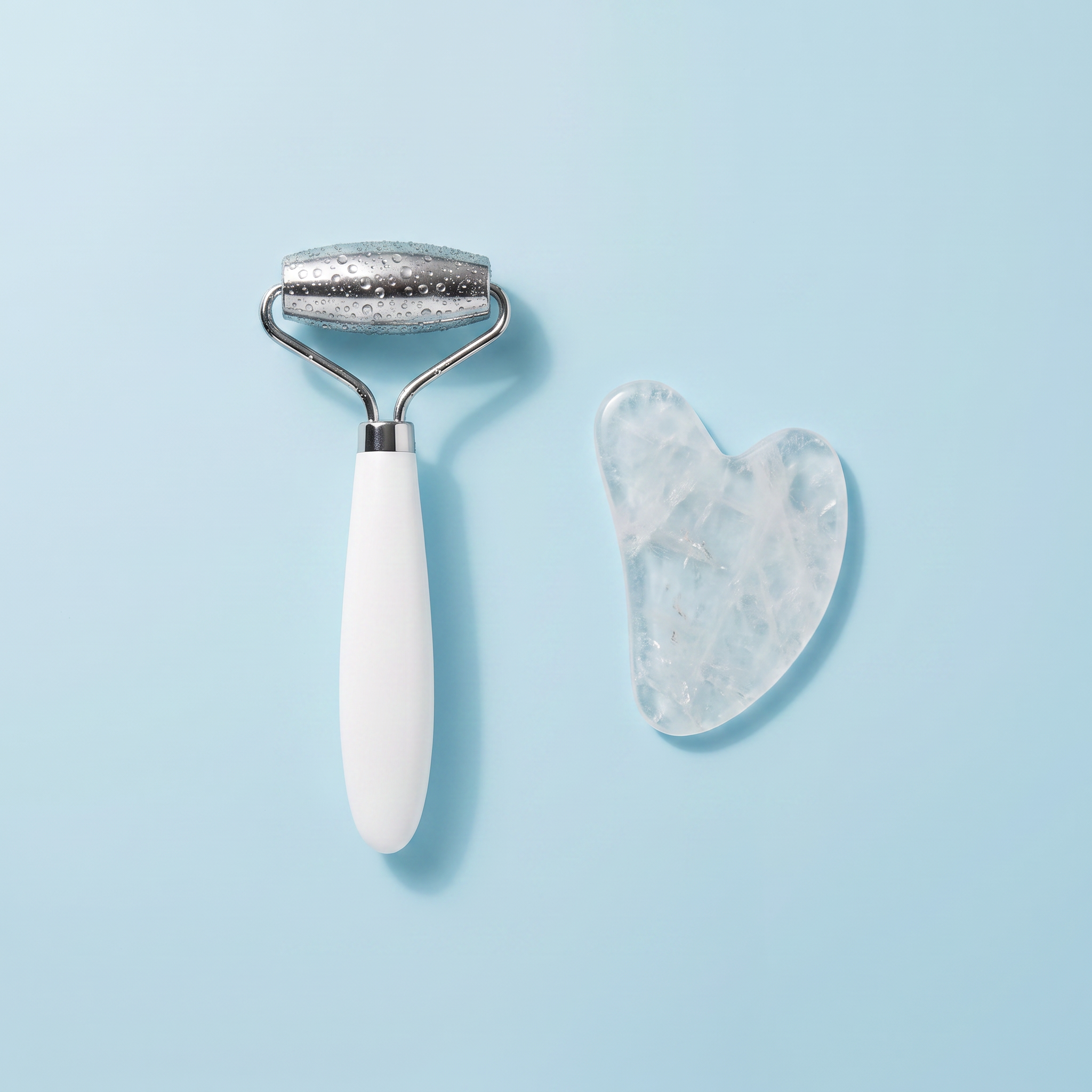 Kit Rituale Fresh visto dall'alto: roller viso in acciaio e pietra gua sha in quarzo su superficie azzurro ghiaccio
