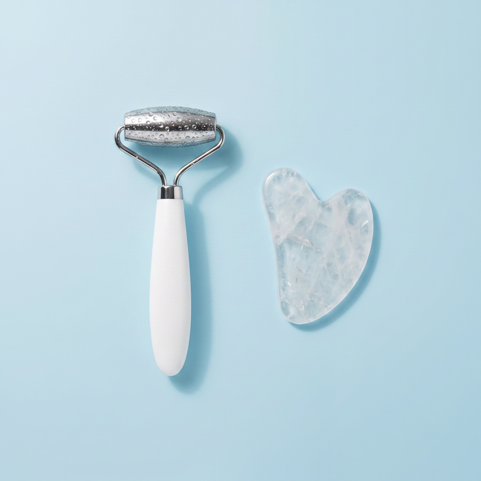 Kit Rituale Fresh visto dall'alto: roller viso in acciaio e pietra gua sha in quarzo su superficie azzurro ghiaccio